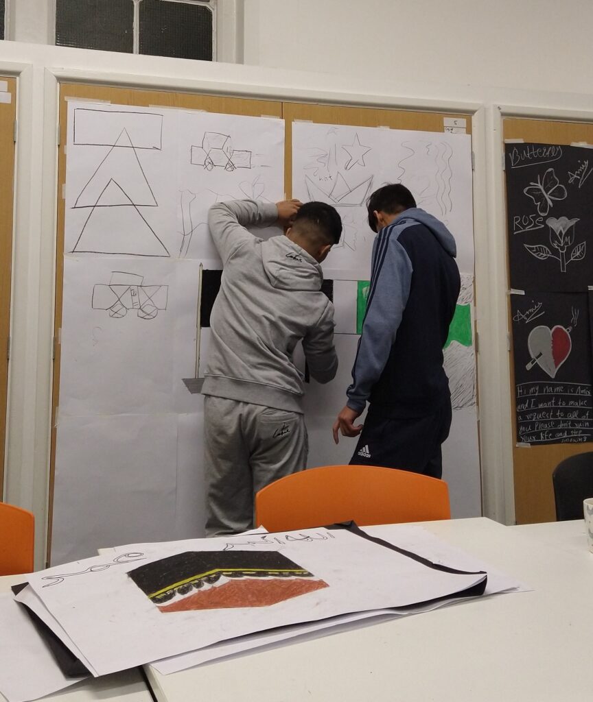 Two male service users work on a drawing of a flag on a large work of art taped to the wall during the weekly After18 art and photography club